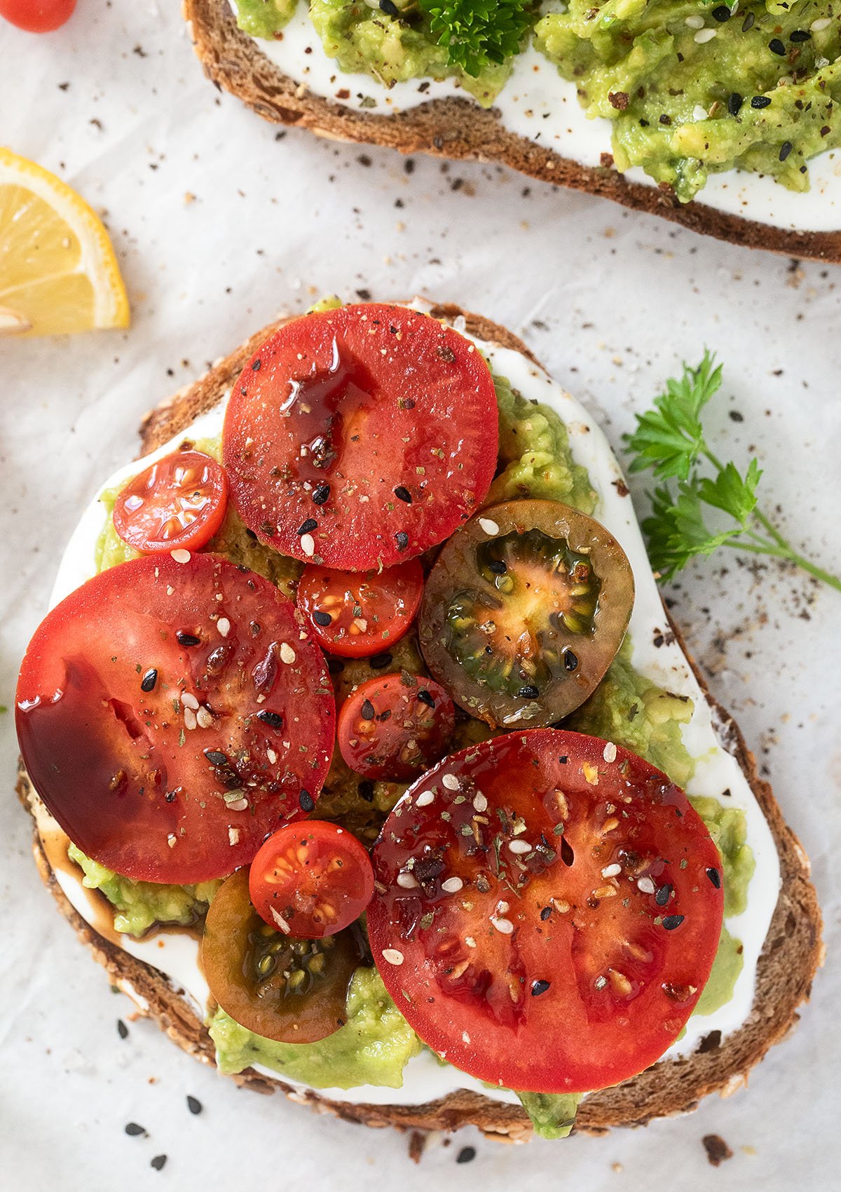 close up of one slice bread topped with tomato slices, balsamic and seeds.