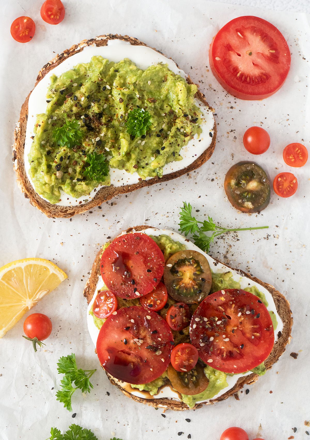 overhead view of two bread slices topped with cottage cheese and avocado and with tomato slices, small tomatoes around them.