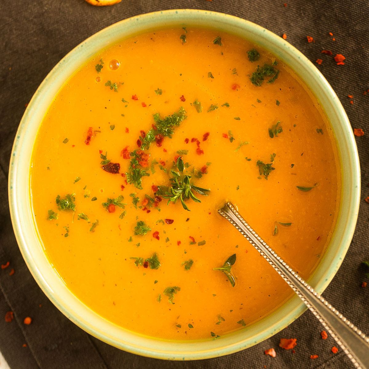 bowl of pumpkin soup without cream sprinkled with chili and parsley.