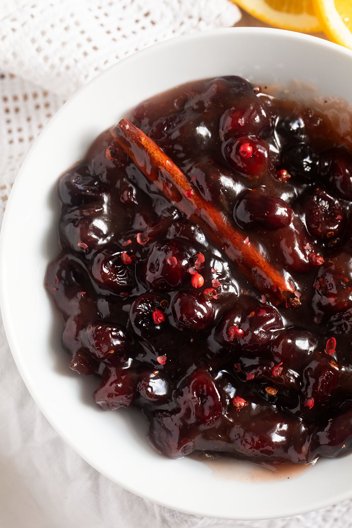 close up of glossy cranberry sauce made with dried fruit in a small white bowl.