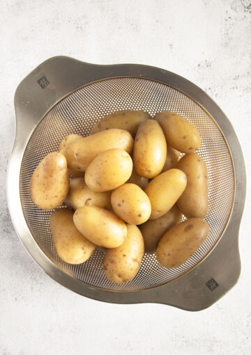 boiled small potatoes steaming in a sieve.