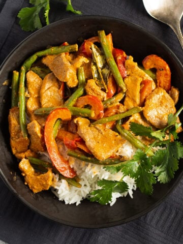 thai pork curry served in a black bowl over rice.