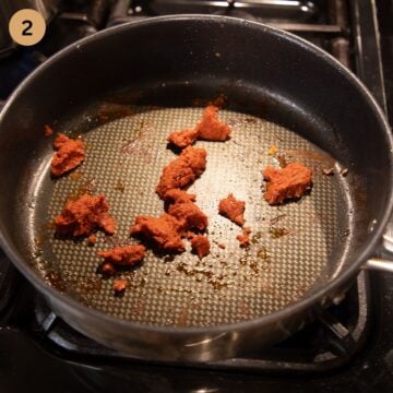 frying red curry paste in a large pan.