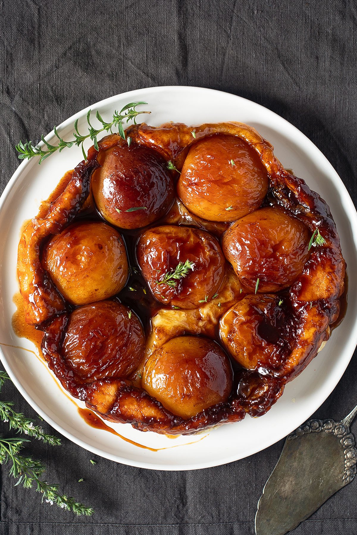 peach tarte tatin with puff pastry on a white plate with a few sprigs of thyme around it.