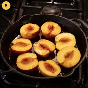 peach halves cut side up placed in caramel sauce in a cast iron pan.