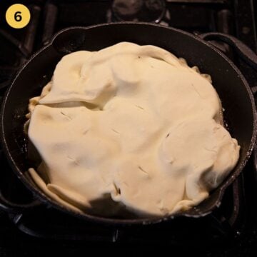 puff pastry covering peach halves in a small cast iron skillet.