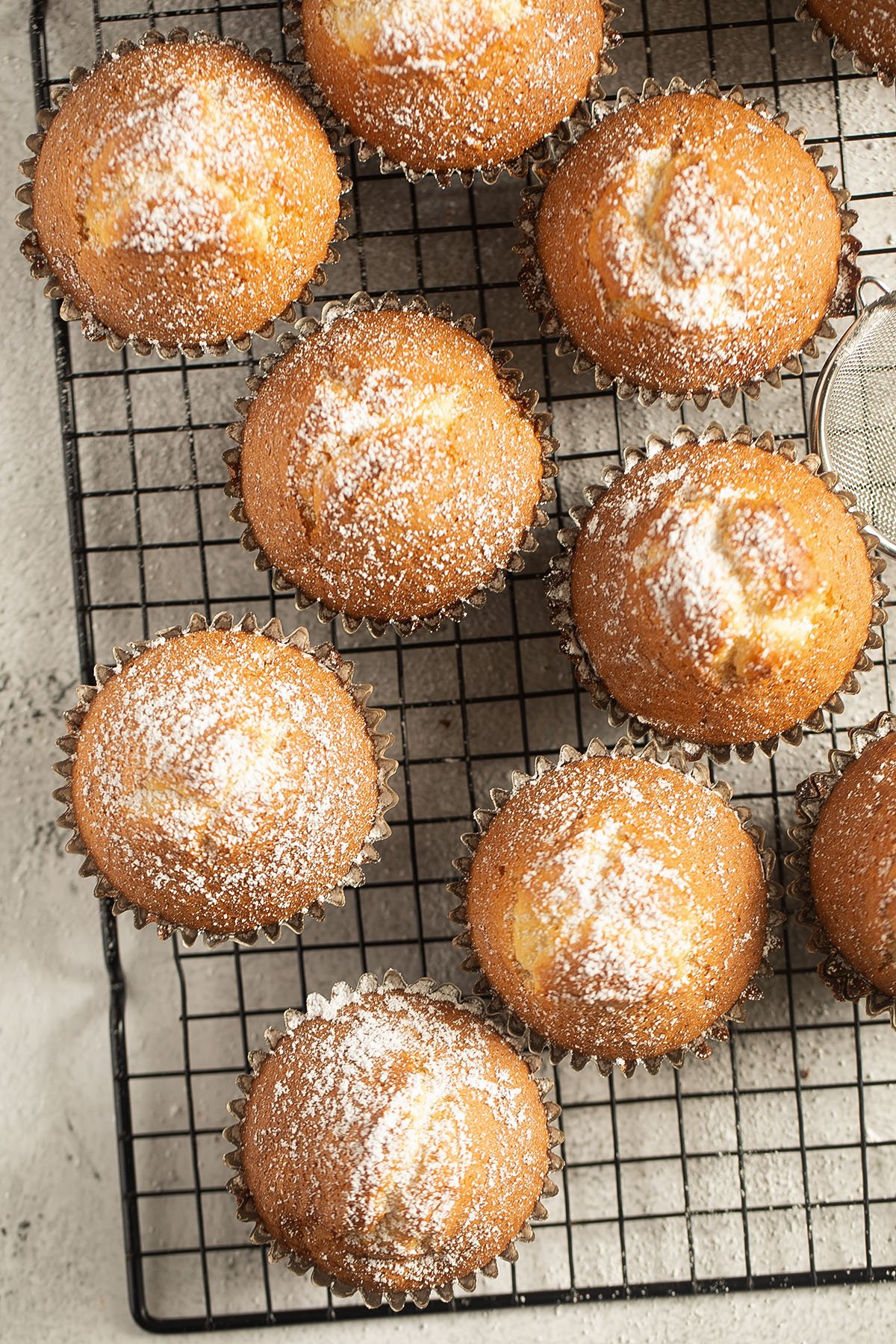 many muffins sprinkled with icing sugar on a wire rack.