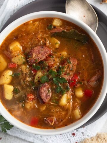 bowl of sauerkraut sausage soup with a spoon beside it.