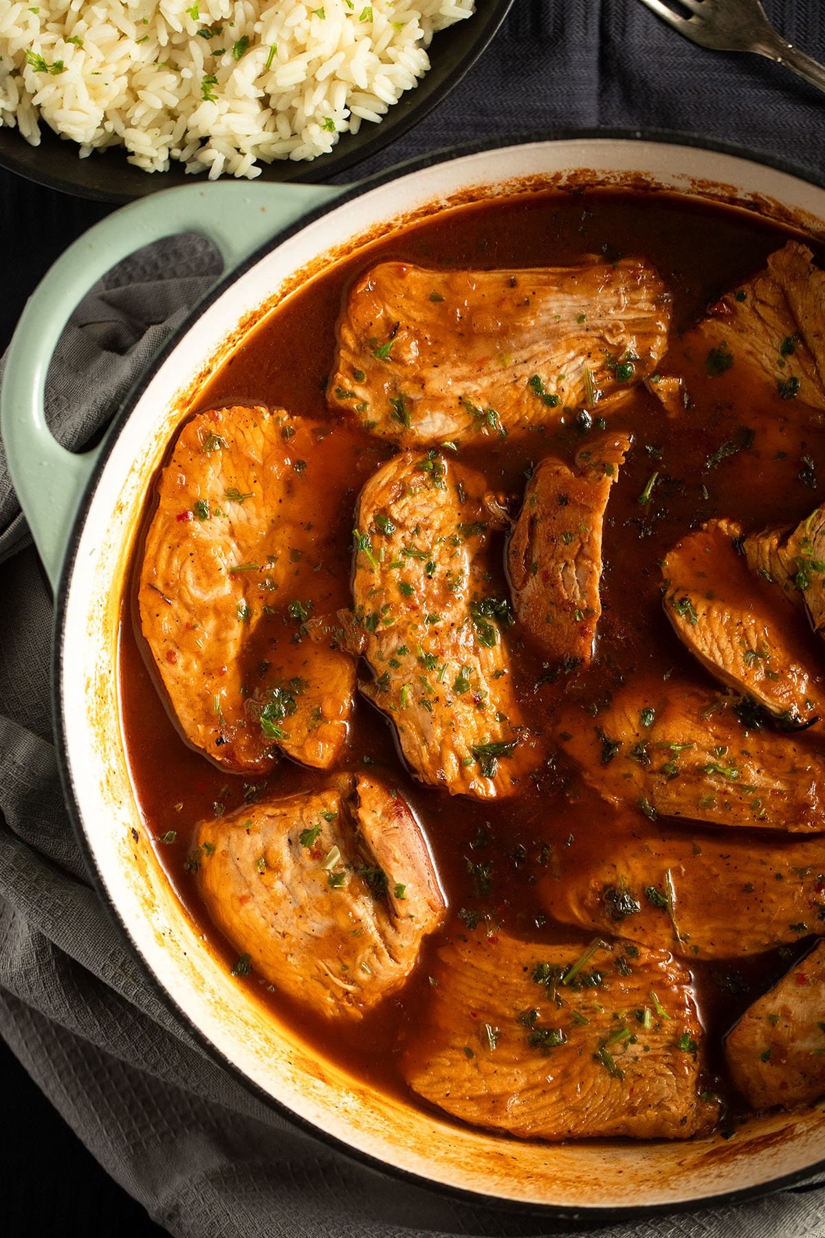 sliced turkey cooked in sauce in a large pot, a bowl of rice beside it.