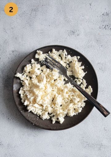 crumbling feta with a fork on a small dark plate.