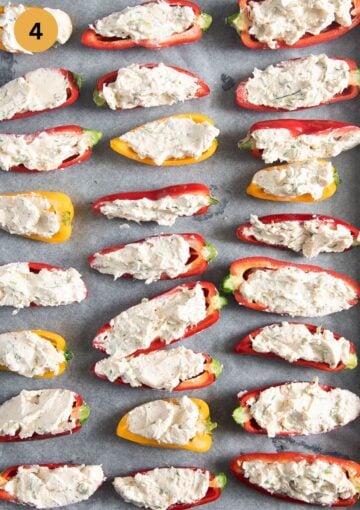 many mini peppers halves stuffed with cheese before baking on a baking sheet.