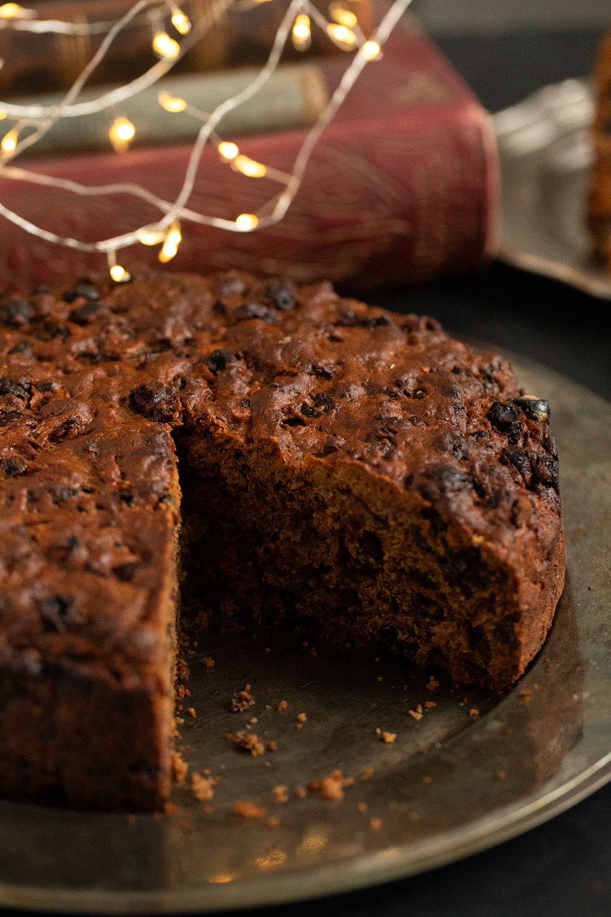 large fruit cake with pineapple and mixed fruit on a platter, with christmas lights above it.