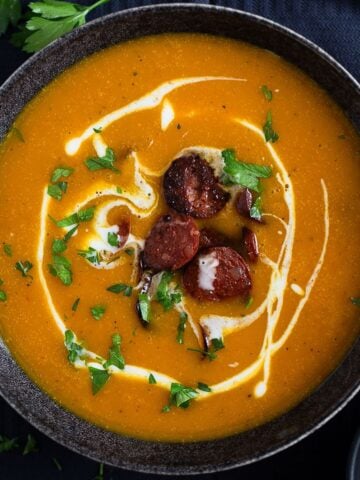 chorizo and pumpkin soup drizzled with cream and sprinkled wiht parsley in a bowl.