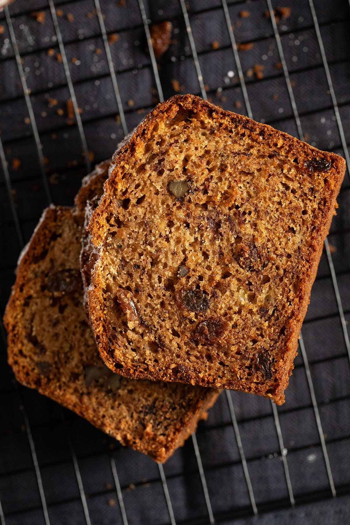 two slices of banana bread with raisins on a wire rack.