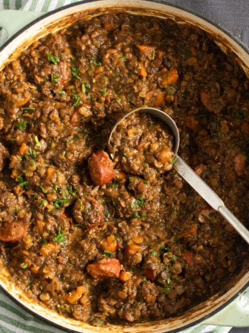 lentil and chorizo stew in a large dutch oven with a ladle spoon in it.