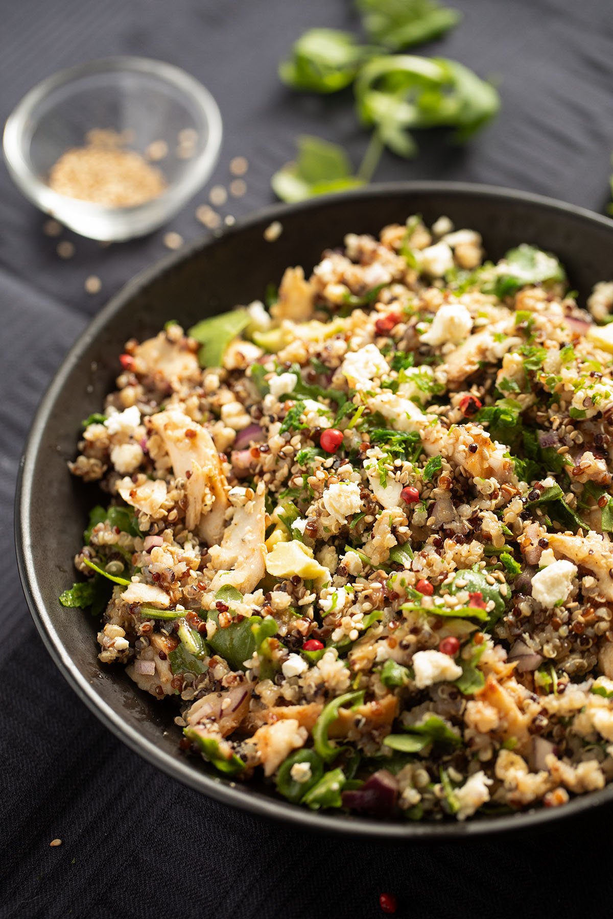 quinoa bowl with salmon, arugula, and avocado, a small bowl with sesame seeds behind it.