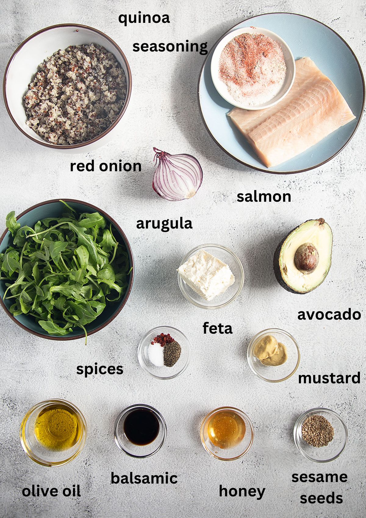 labeled ingredients for making salad with quinoa, salmon, arugula, avocado, and feta.