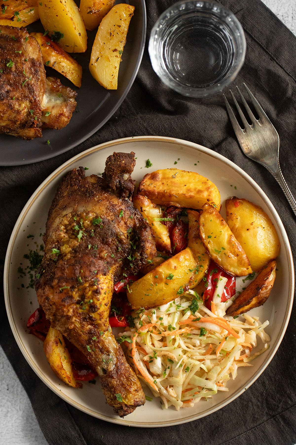one chicken quarter, oven-baked potatoes and coleslaw on a plate.