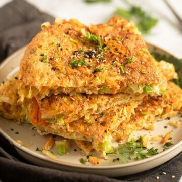 thick slices of cabbage omelette stapled on a plate and sprinkled with herbs and sesame seeds.