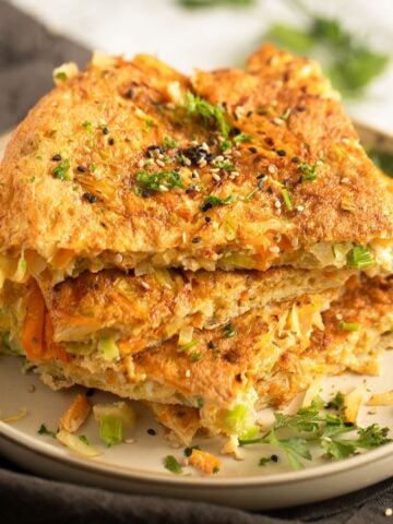 thick slices of cabbage omelette stapled on a plate and sprinkled with herbs and sesame seeds.