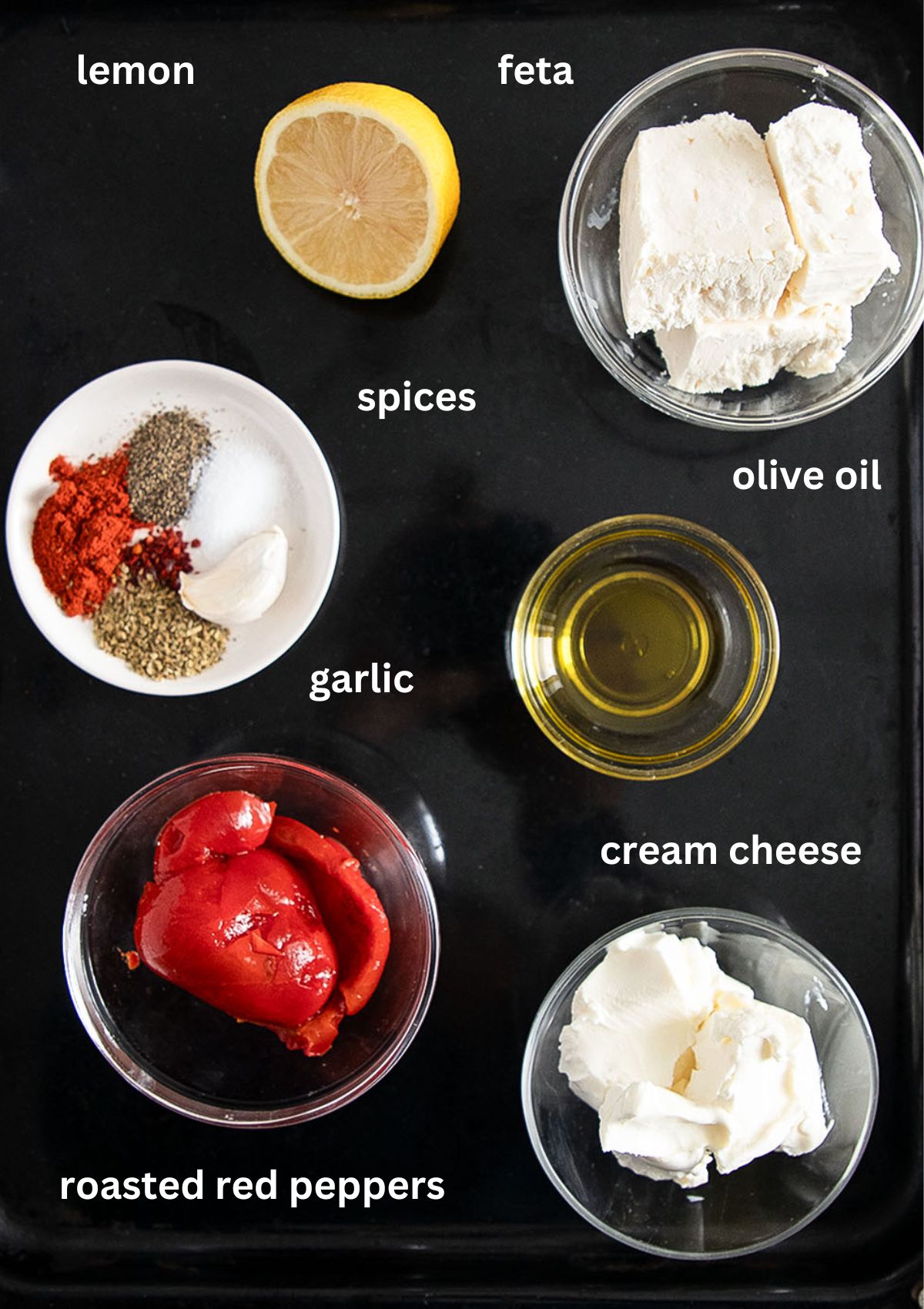 labeled ingredients for making greek dip with feta, roasted red peppers, cream cheese, spices and oil.