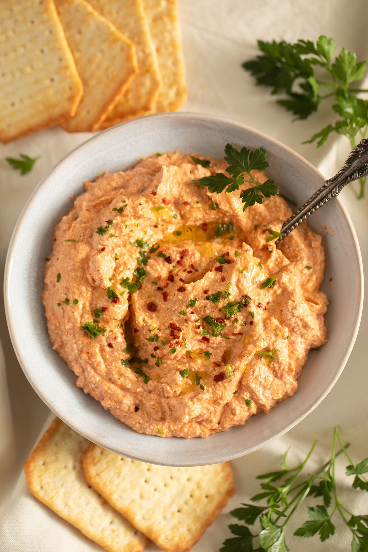 creamy dip with roasted red peppers, feta and cream cheese in a bowl with a spoon in it.