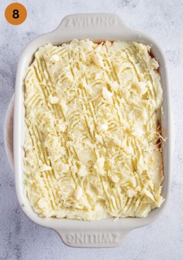 unbaked cottage pie covered with mashed potatoes and dotted with butter in a baking dish.