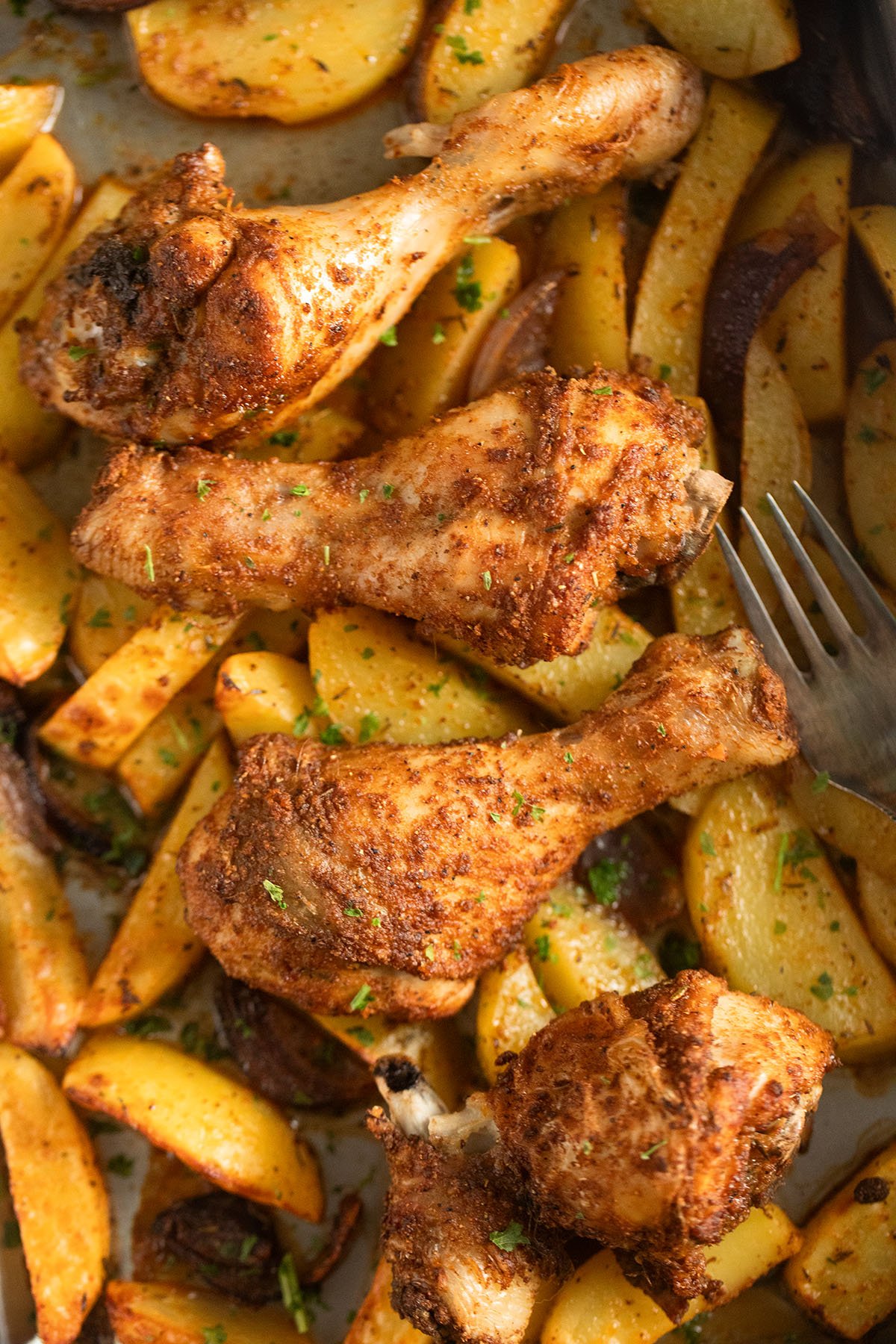 four chicken drumsticks baked on potato wedges and a fork.