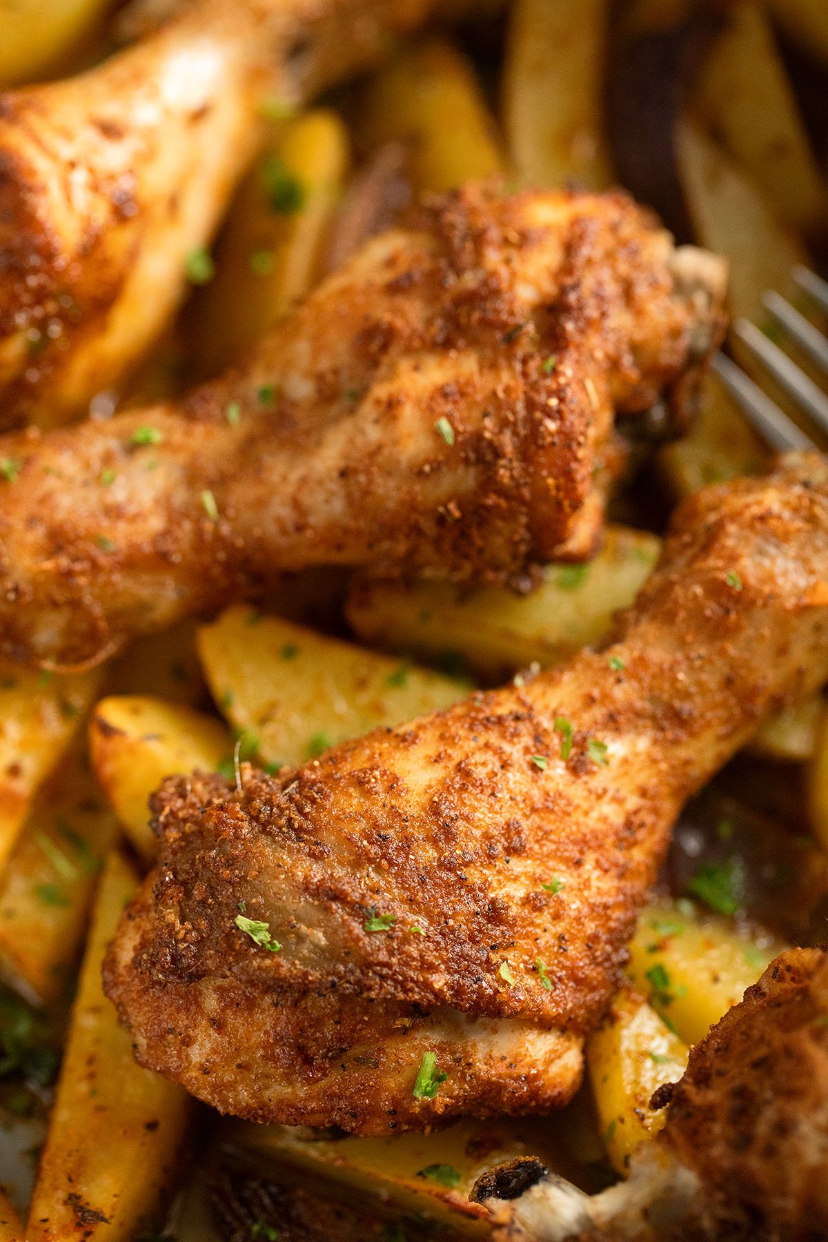 two roasted golden drumsticks on potatoes in a roasting pan.