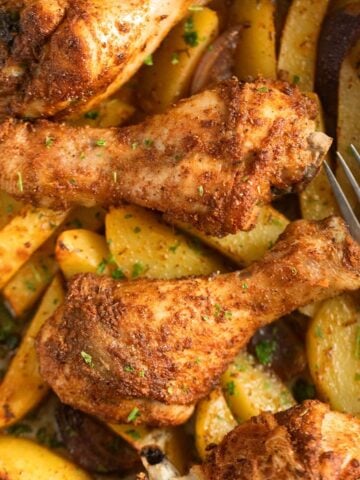 one dish drumsticks and potatoes with a fork in a baking dish.