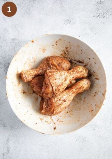 four seasoned chicken drumsticks in a bowl before roasting.