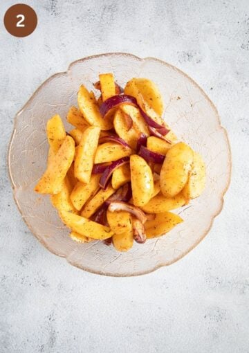 raw potato wedges and red onion slices seasoned in a large bowl.