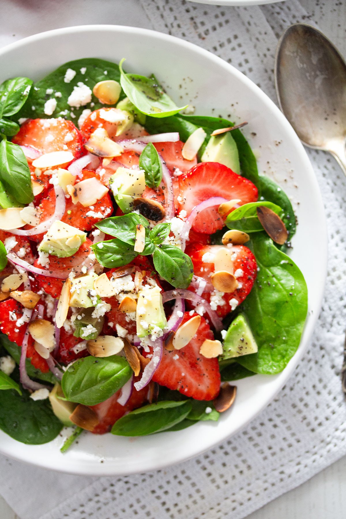 salad with strawberries, goat cheese, spinach and avocado in a bowl, a spoon beside it.