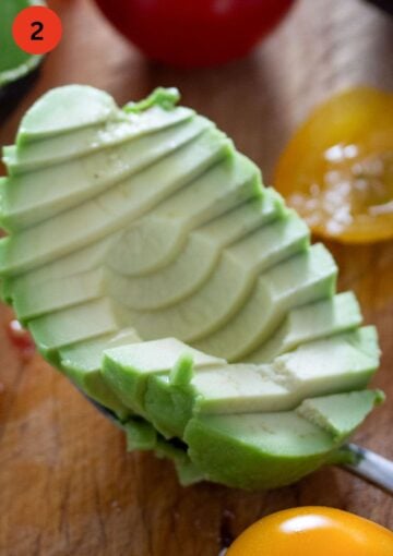 slice avocado half held by a spoon.