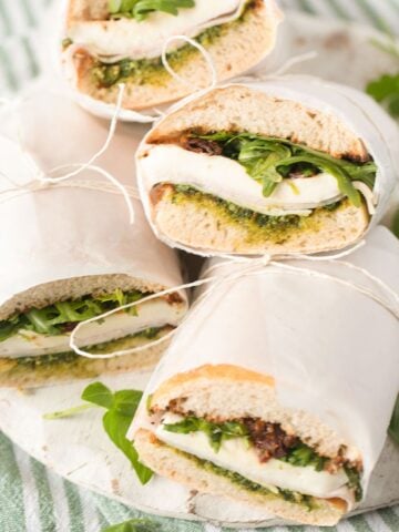 four pieces of ciabatta sandwich and basil leaves scattered around them.
