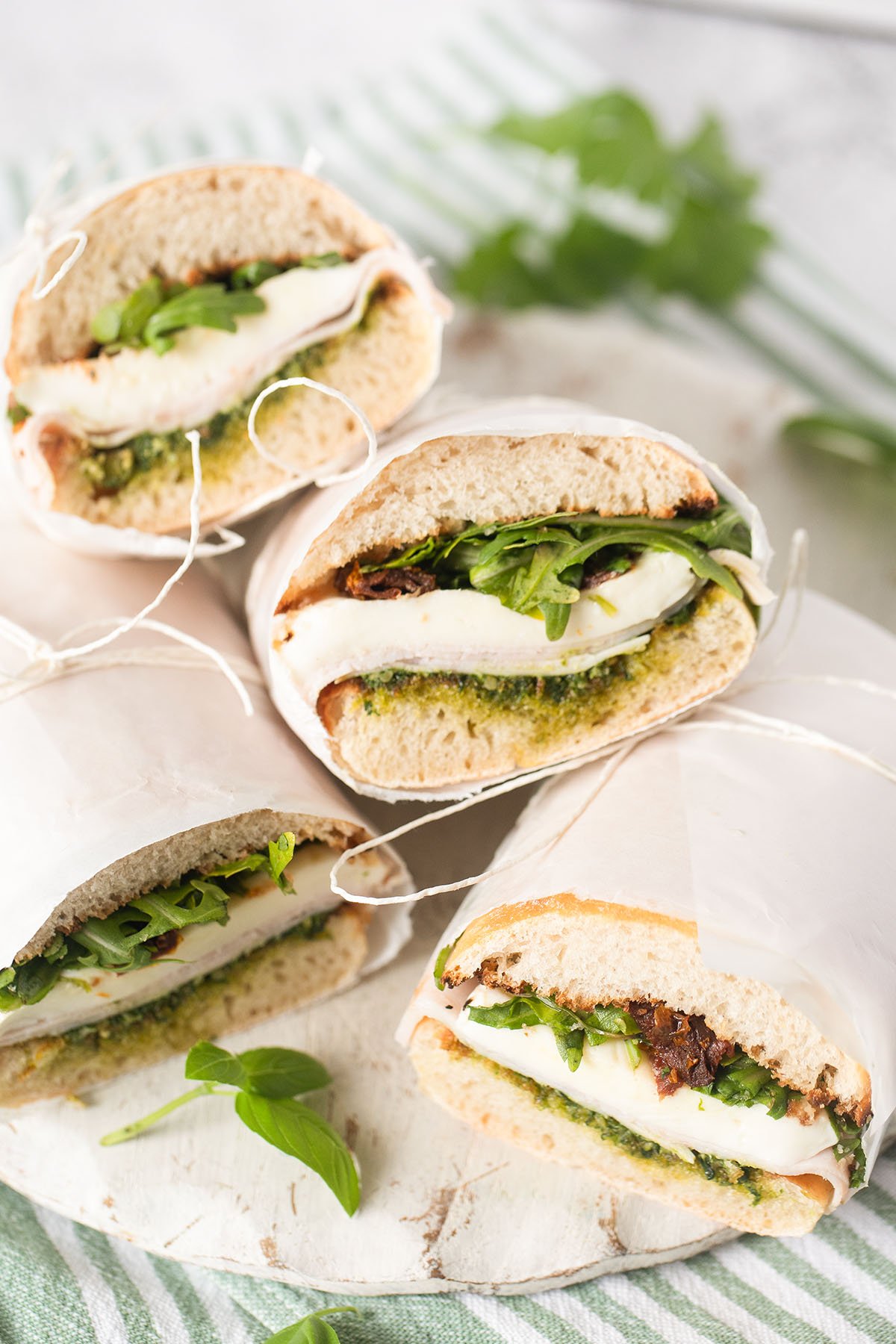 four sandwiches with arugula and mozzarellla on a cutting board.