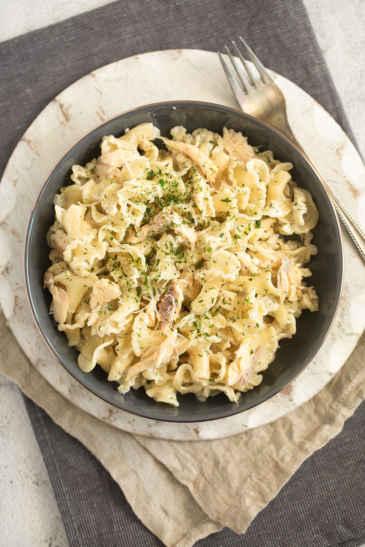 smoked trout pasta in a bowl on a cutting board with a fork beside it.