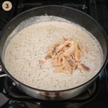 adding flaked smoked trout to cream sauce in a saucepan.