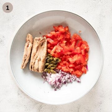 sardines, chopped tomatoes, capers, onion and garlic in a bowl.