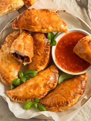puff pastry empanadas on a plate served with salsa and basil leaves.
