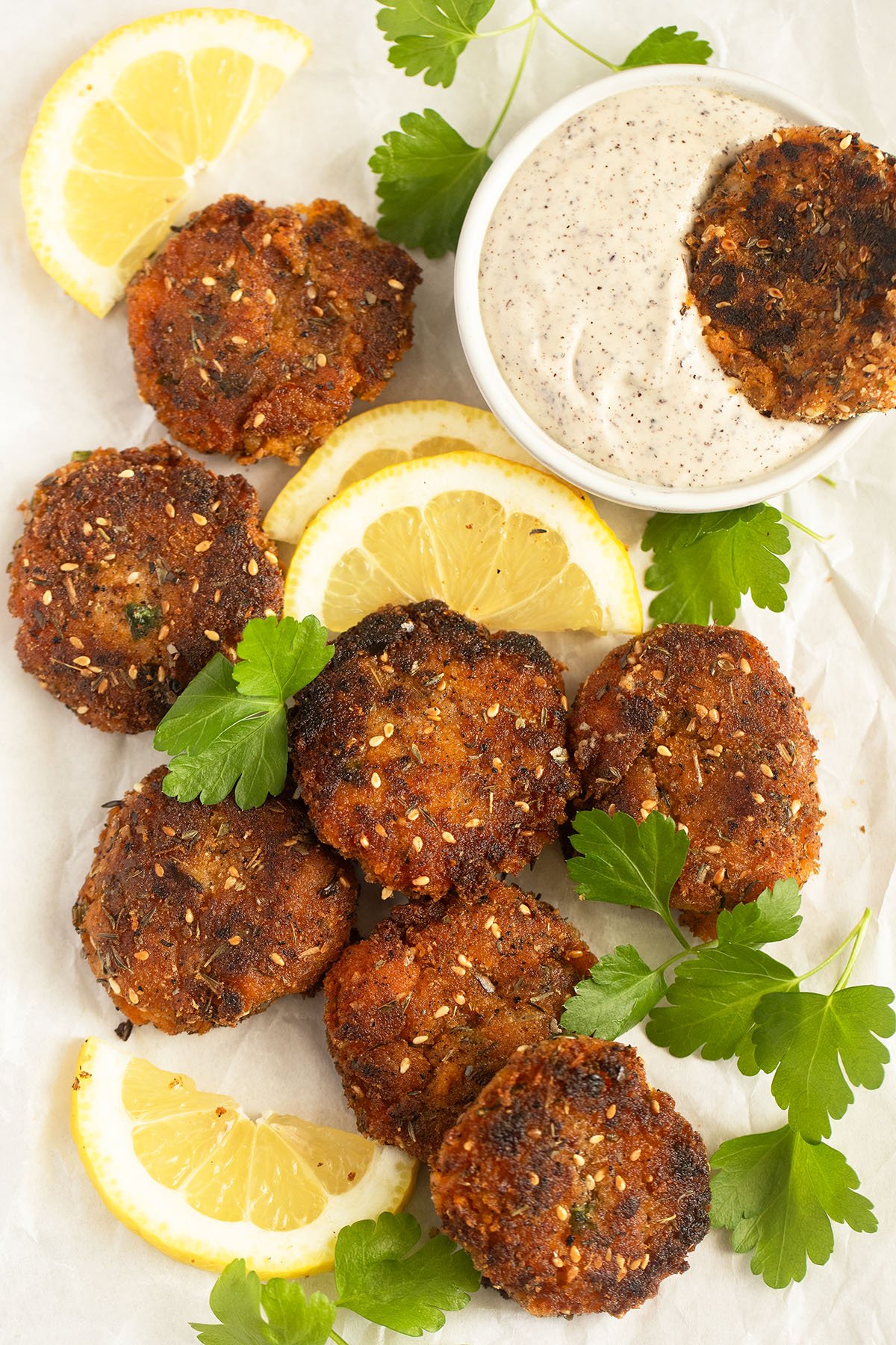 many sweet potato and shrimp cakes served with tahini sauce in a bowl, lemon slices and cilantro.