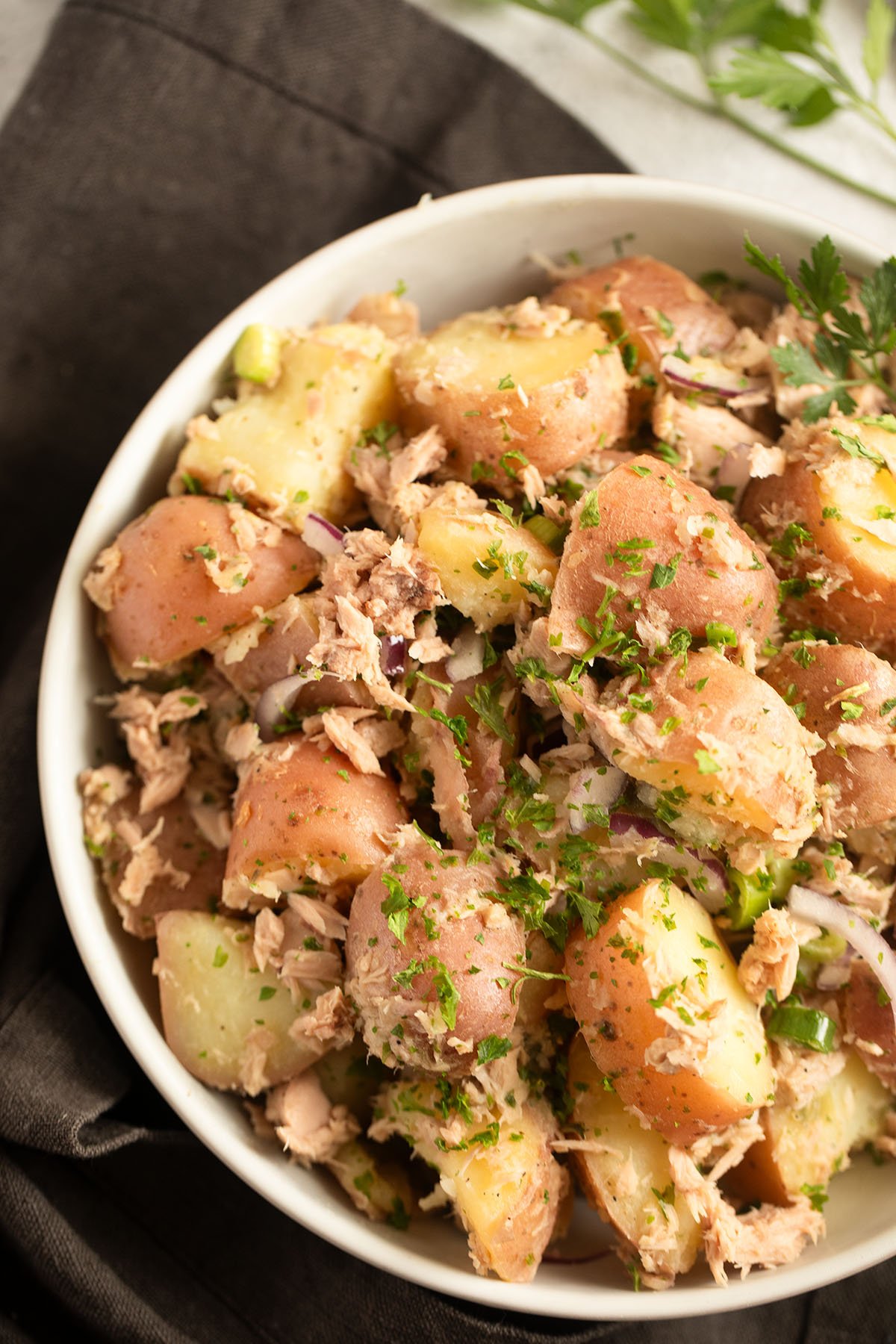 tuna and potato salad sprinkled with herbs in a bowl.