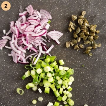 chopped red onions, green onions and capers on a cutting board.