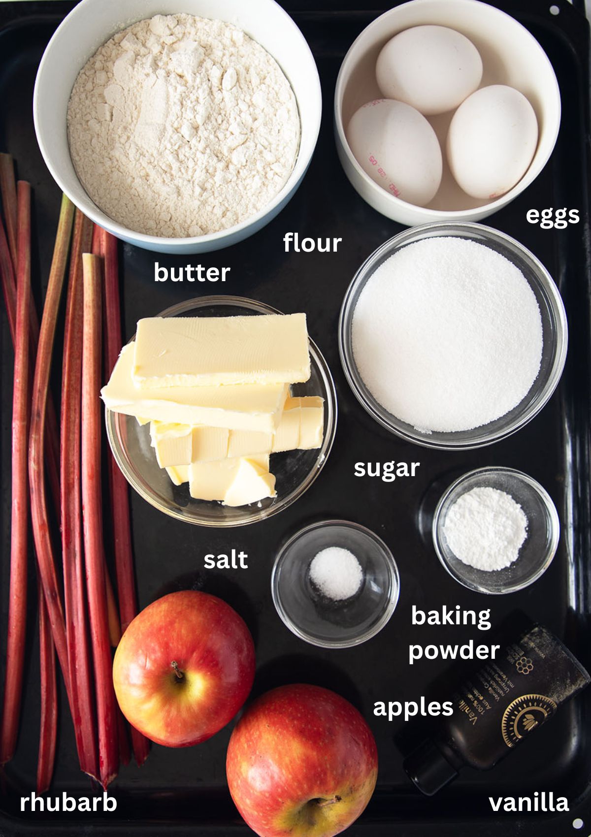 labeled ingredients for making cake with rhubarb, apples, butter, sugar, eggs, flour, and baking powder.
