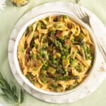 asparagus pea pasta in a bowl on a round cutting board with a fork beside it.