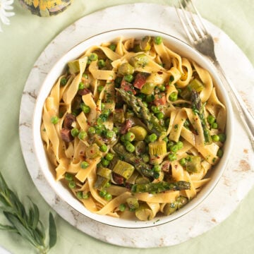 asparagus pea pasta in a bowl on a round cutting board with a fork beside it.
