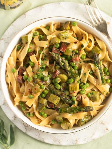 asparagus pea pasta in a bowl on a round cutting board with a fork beside it.