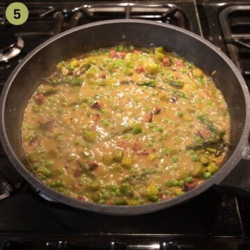 simmering pasta sauce wiht asparagus adn peas in a skillet.