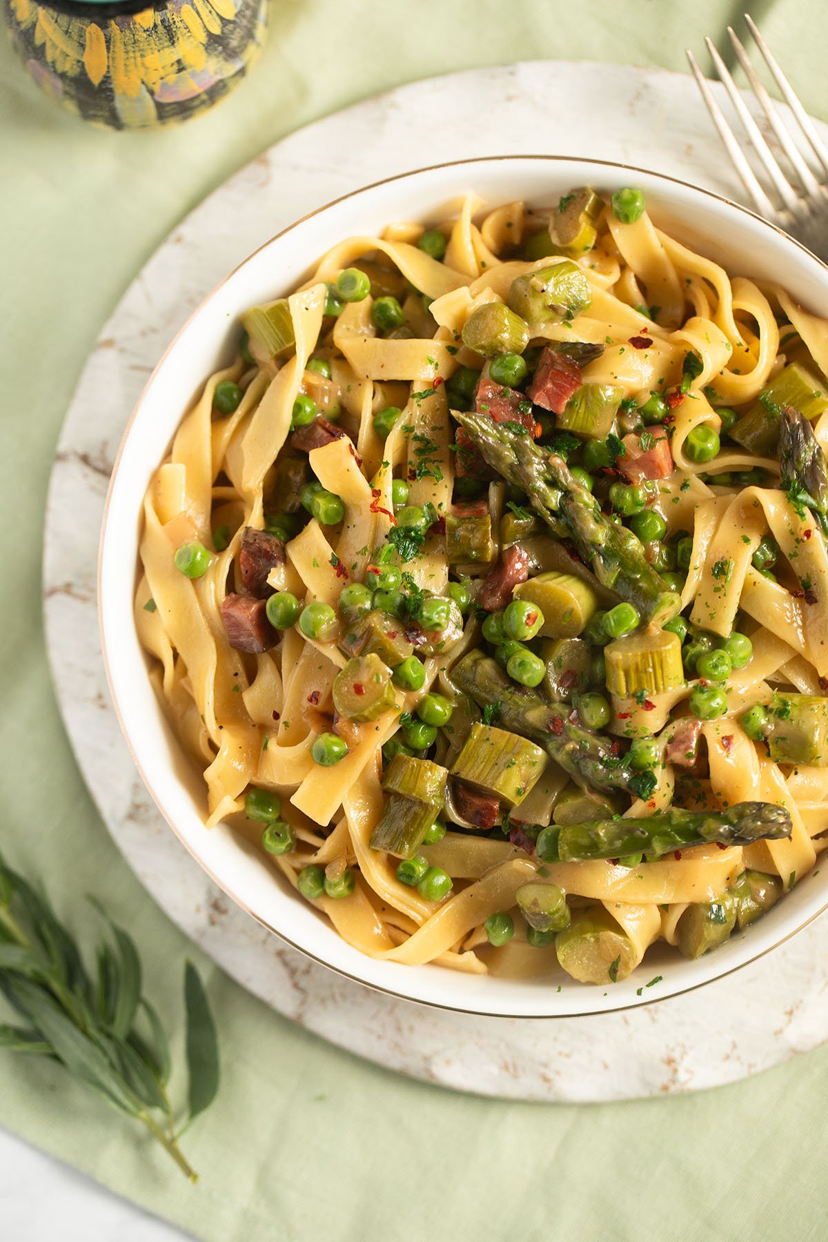 asparagus and pea pasta with bacon and tarragon in a bowl on a white cutting board.
