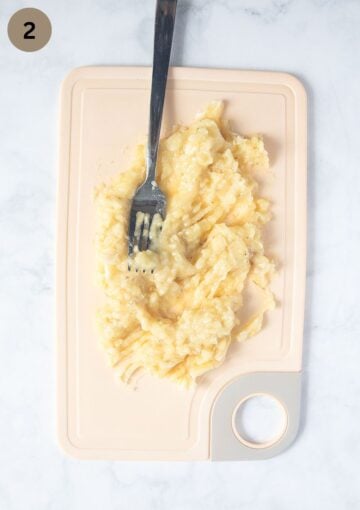 mashing bananas with a fork on a cutting board.